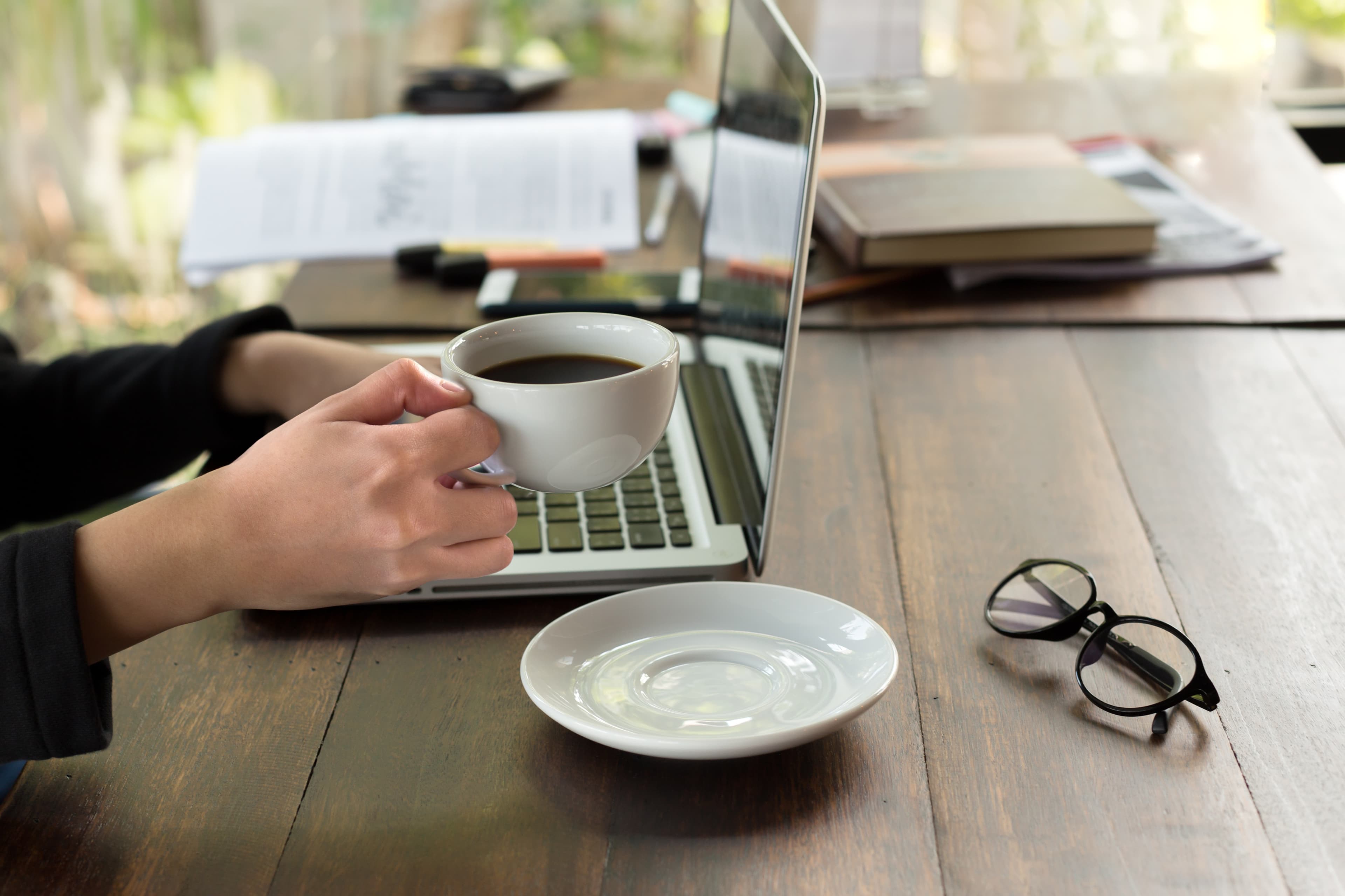 Profesional trabajando en laptop con café y lentes en escritorio